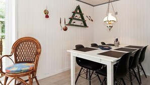 A dining area with a white table, black chairs, and a wicker chair with a colorful cushion.