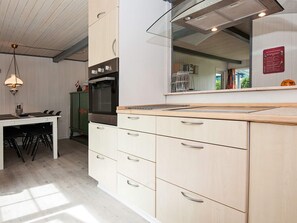 A modern kitchen with a built-in oven, a dining table with chairs, and a large mirror above the countertop. - 4 Person Holiday Home in Hejls (Hejls)