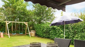 A patio with a swing set, a table with chairs, and a large umbrella. - 4 Person Holiday Home in Hejls (Hejls)