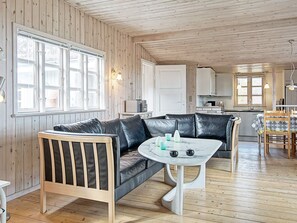 A cozy cabin interior with a wooden floor, a leather sofa, a small white table, and a kitchen area in the background. - 6 Person Holiday Home in Nexo (Nexø)