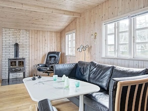 Une pièce chaleureuse avec un canapé en cuir, une table blanche, une cheminée en briques et des murs en bois.