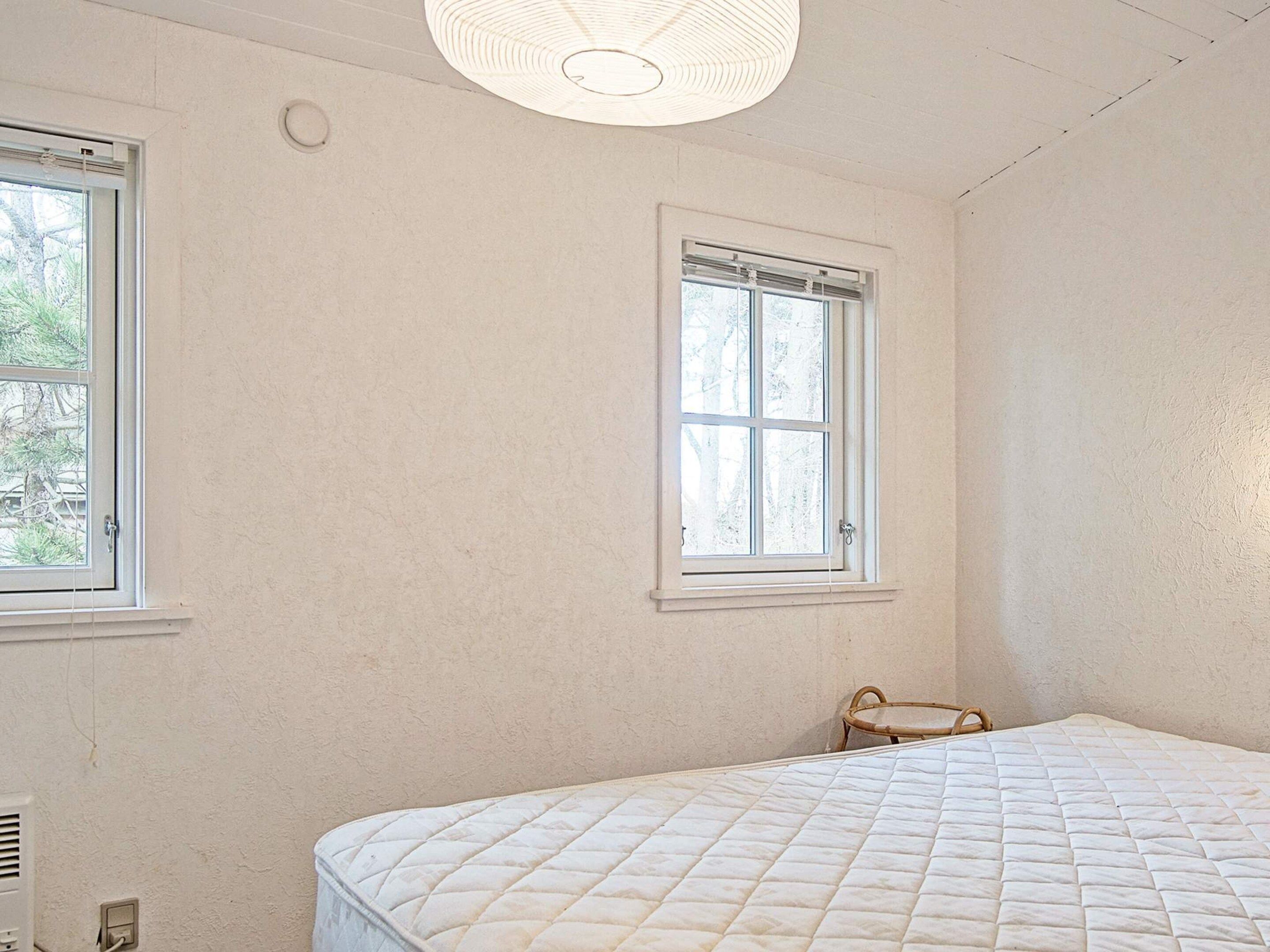 Un dormitorio con cama, dos ventanas y una lámpara en el techo.