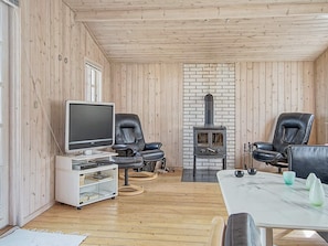 A cozy living room with a television, two leather chairs, a white table with decorative items, and a wood-burning stove. - 6 Person Holiday Home in Nexo (Nexø)