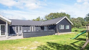 Een tweelaags huis met een donkere gevel, een overdekt terras en een gazon met een speeltuin.