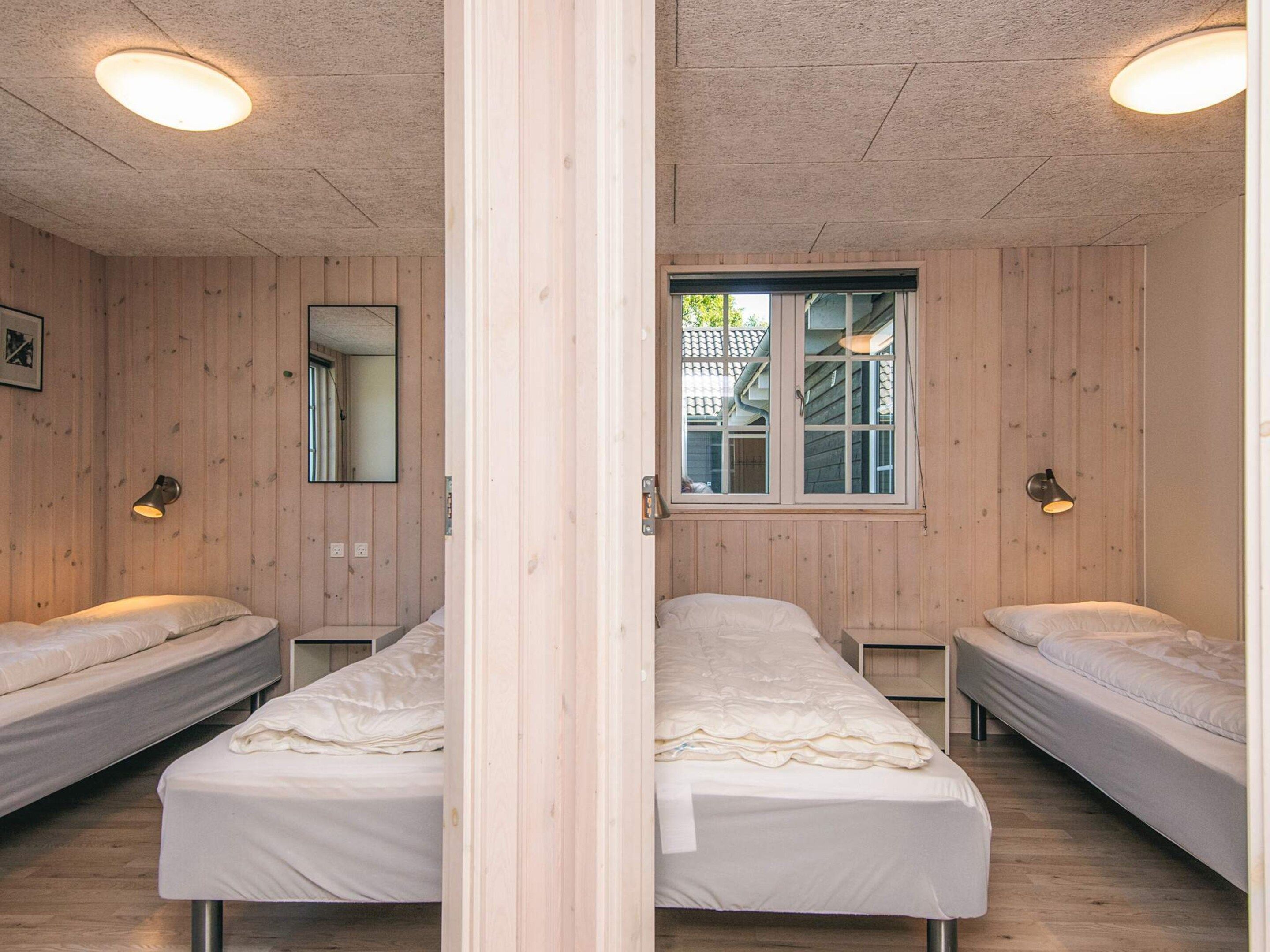 A room with two single beds, wooden walls, a window with a view, and a mirror.