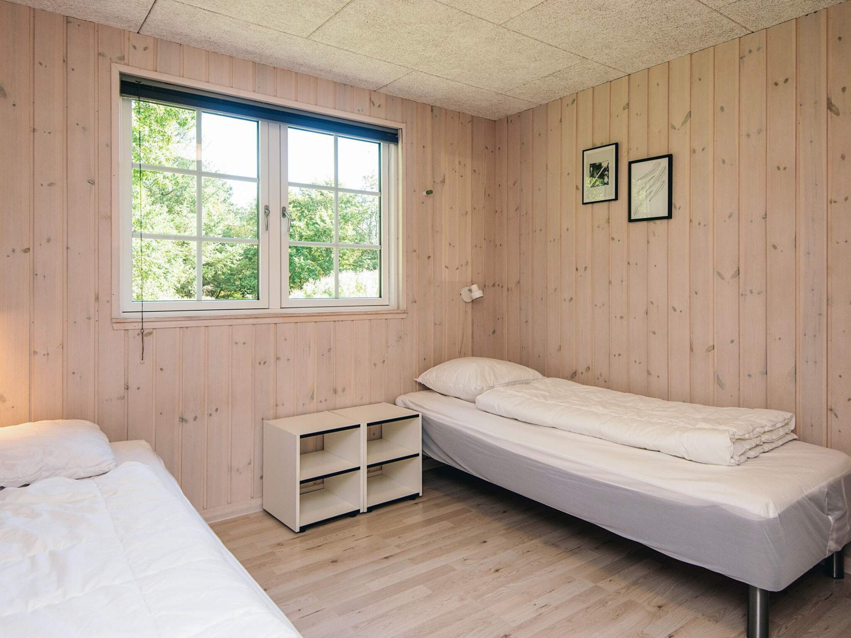 A small, single-bed room with wooden walls, a window, and a bedside table.