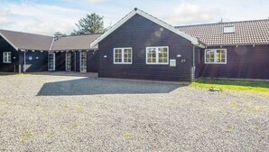 Een rij donkere houten gebouwen met een grindpad en een heldere lucht.