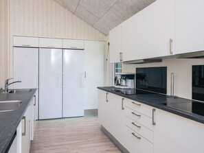 A modern kitchen with white cabinets, a black countertop, and stainless steel appliances. - 5 Star Holiday Home in Blavand (Blavand)