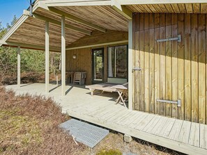 A wooden cabin with a covered porch, a table, and a bench.