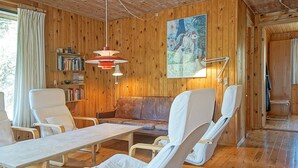Un interior de madera con un sofá, sillas, una mesa y una estantería.
