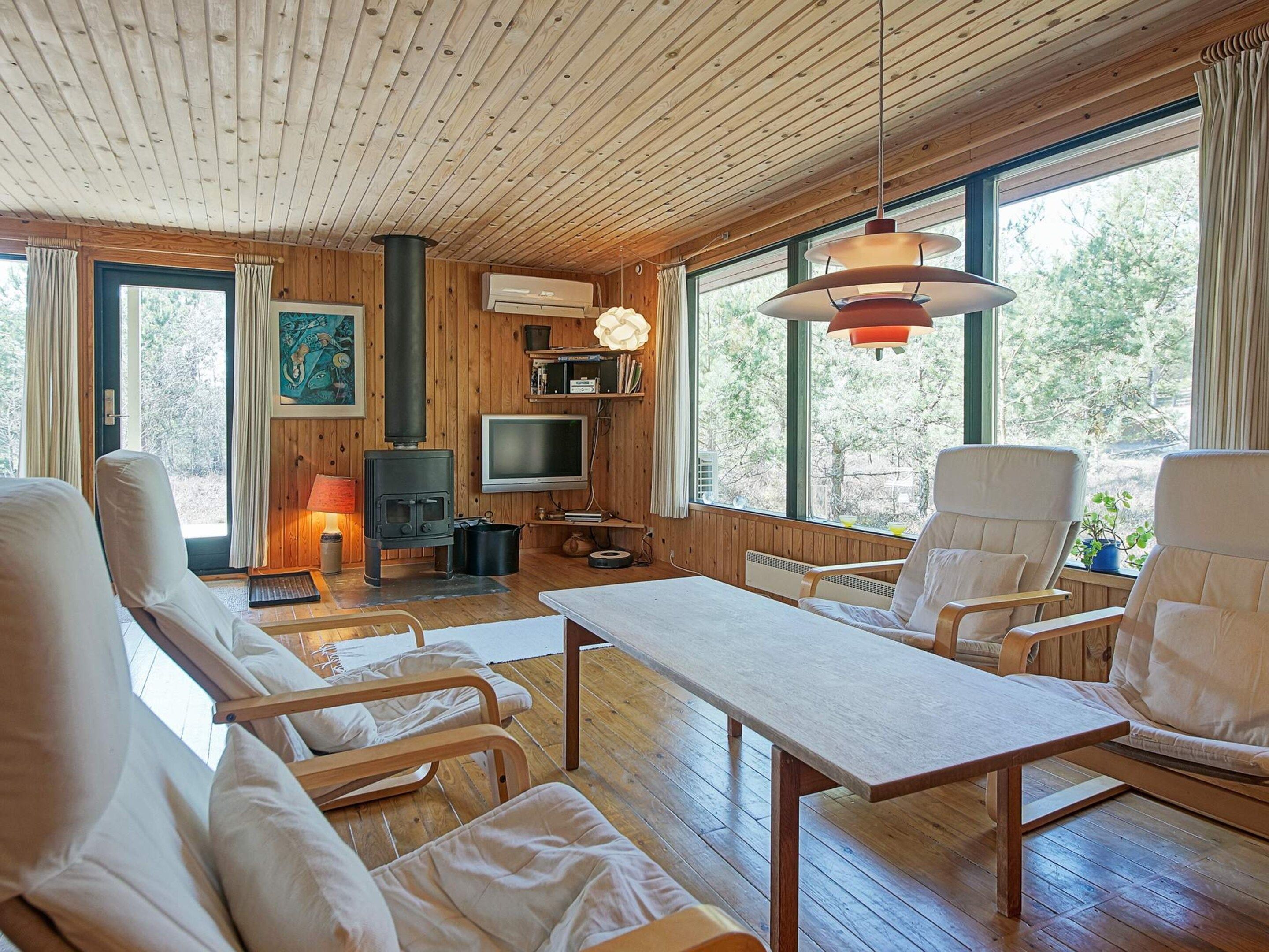 A cozy cabin interior with a wooden ceiling, a fireplace, a television, and comfortable seating.