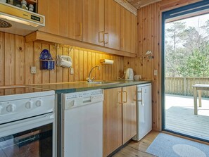 A compact kitchen with wooden cabinets, a built-in oven, a dishwasher, and a sink. - Cozy Holiday Home in Bornholm near Sea (Nexø)