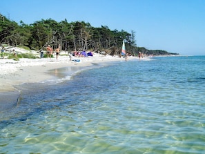 A beach with clear shallow waters, tents, and people walking along the shore.