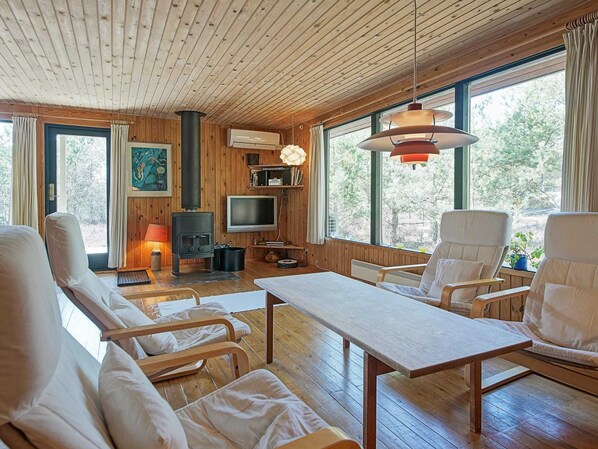 Interior acogedor de una cabaña con paredes de madera, un ventanal grande, chimenea y asientos cómodos.