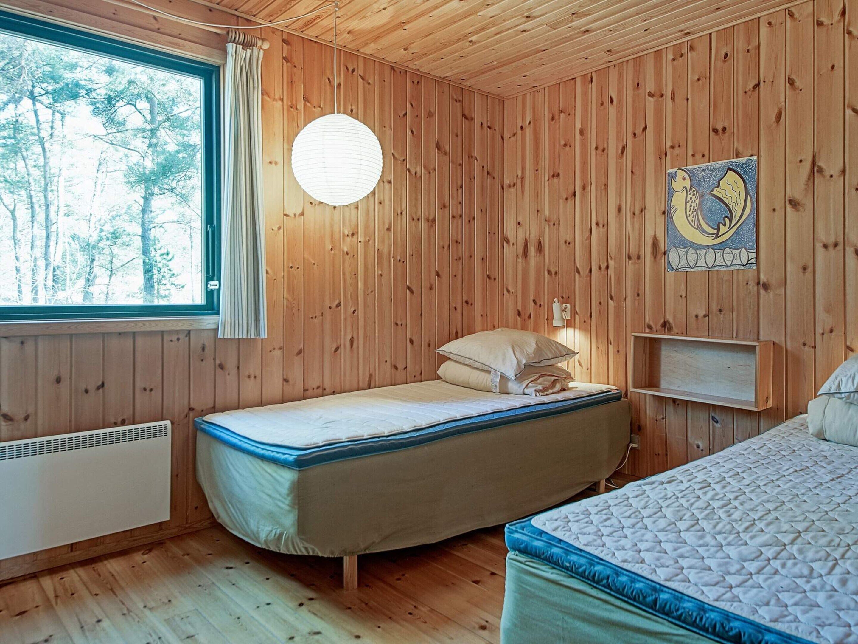 A wooden-paneled room with a bed, a window, and a wall-mounted light fixture.