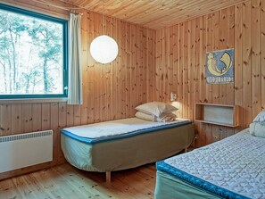 A wooden-paneled room with a bed, a window, and a wall-mounted light fixture.