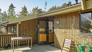 Eine Holzterrasse mit Tisch, Stühlen, einer Tür und einem aufgerollten Gartenschlauch rechts.
