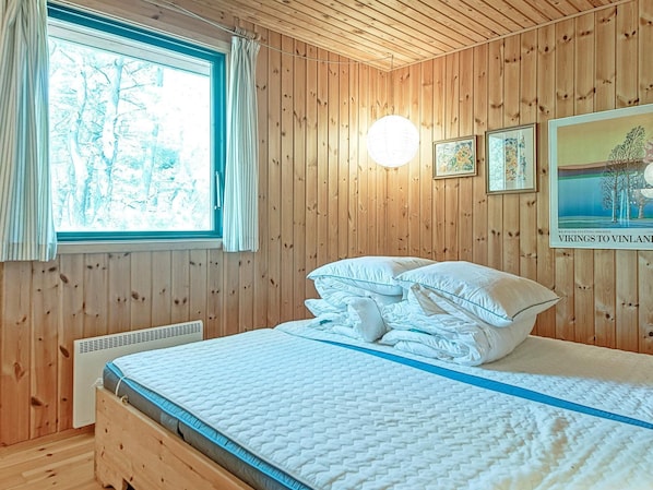 A wooden-paneled room with a bed, a window with curtains, and framed pictures on the wall. - Cozy Holiday Home in Bornholm near Sea (Nexø)