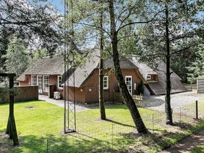 A brick house with a thatched roof, surrounded by trees and a fenced yard.