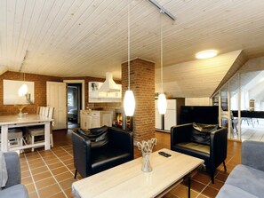 A spacious living area with a fireplace, leather sofas, a dining table, and a kitchen in the background. - 5 Star Holiday Home in Vaeggerlose (Vaeggerlose)