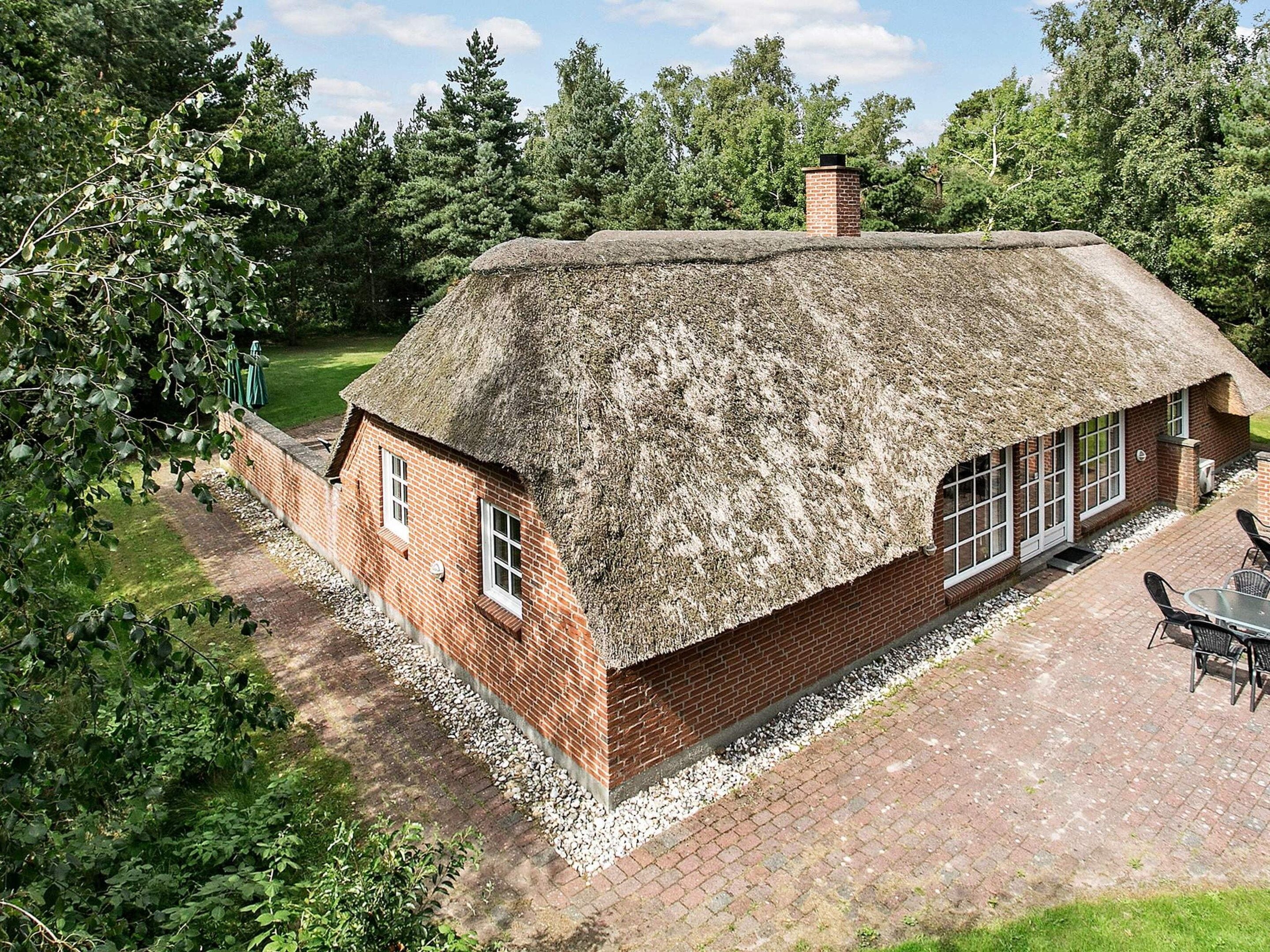 A thatched-roof house with a brick exterior, a paved patio, and a garden area.