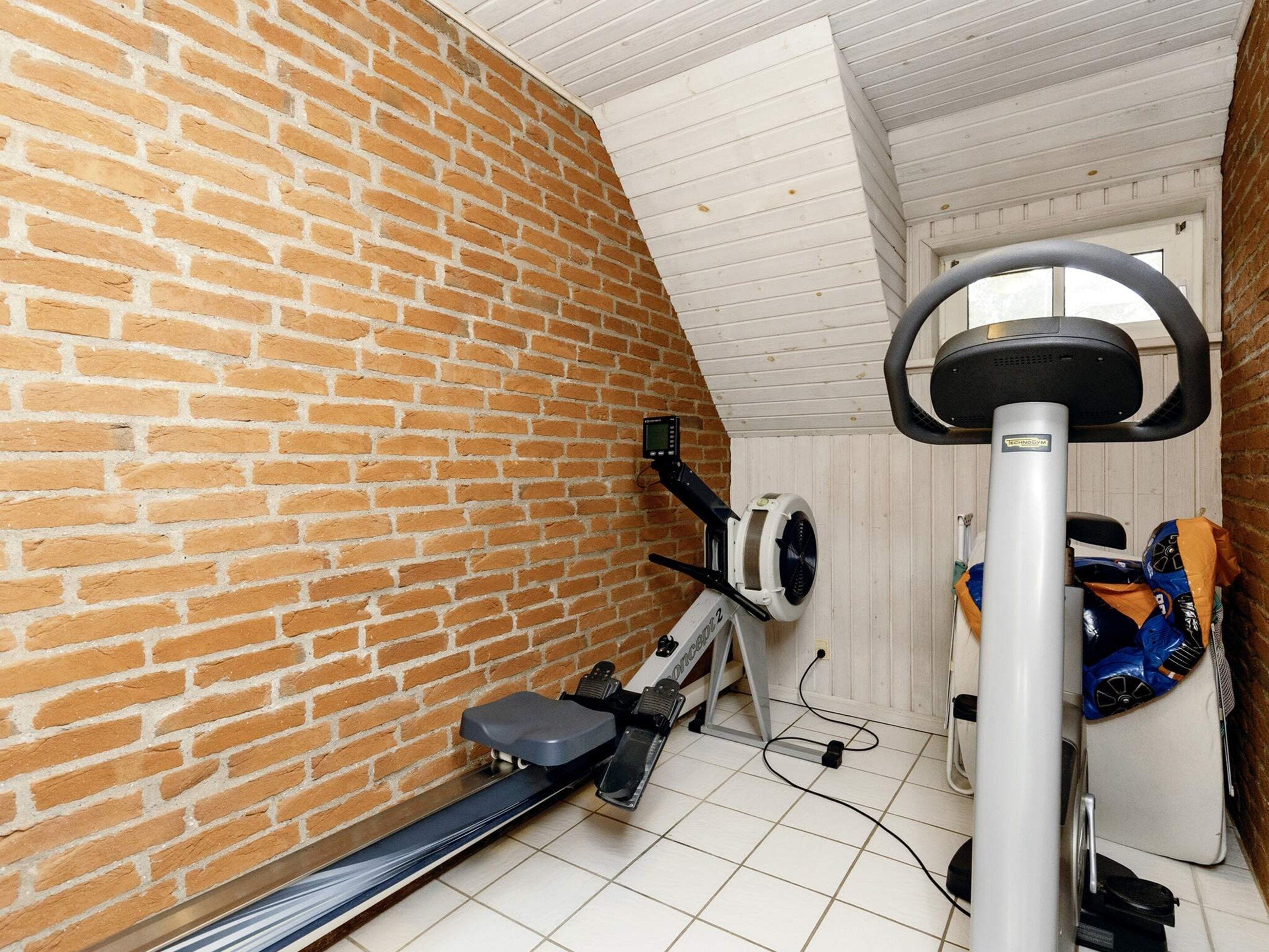 A room with a brick wall, a ceiling fan, a treadmill, and exercise equipment.