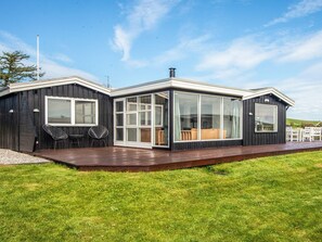 A modern house with a large glass window, a deck, and a grassy lawn.