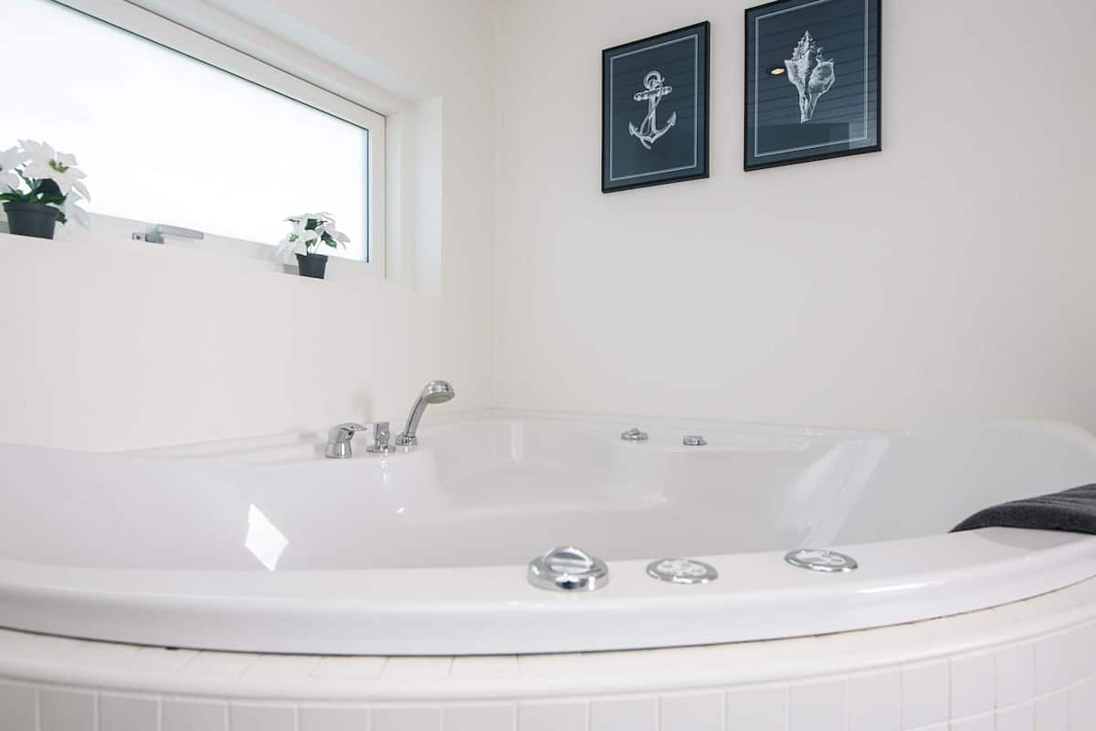 A bathroom with a white bathtub, a window, and two framed pictures on the wall.