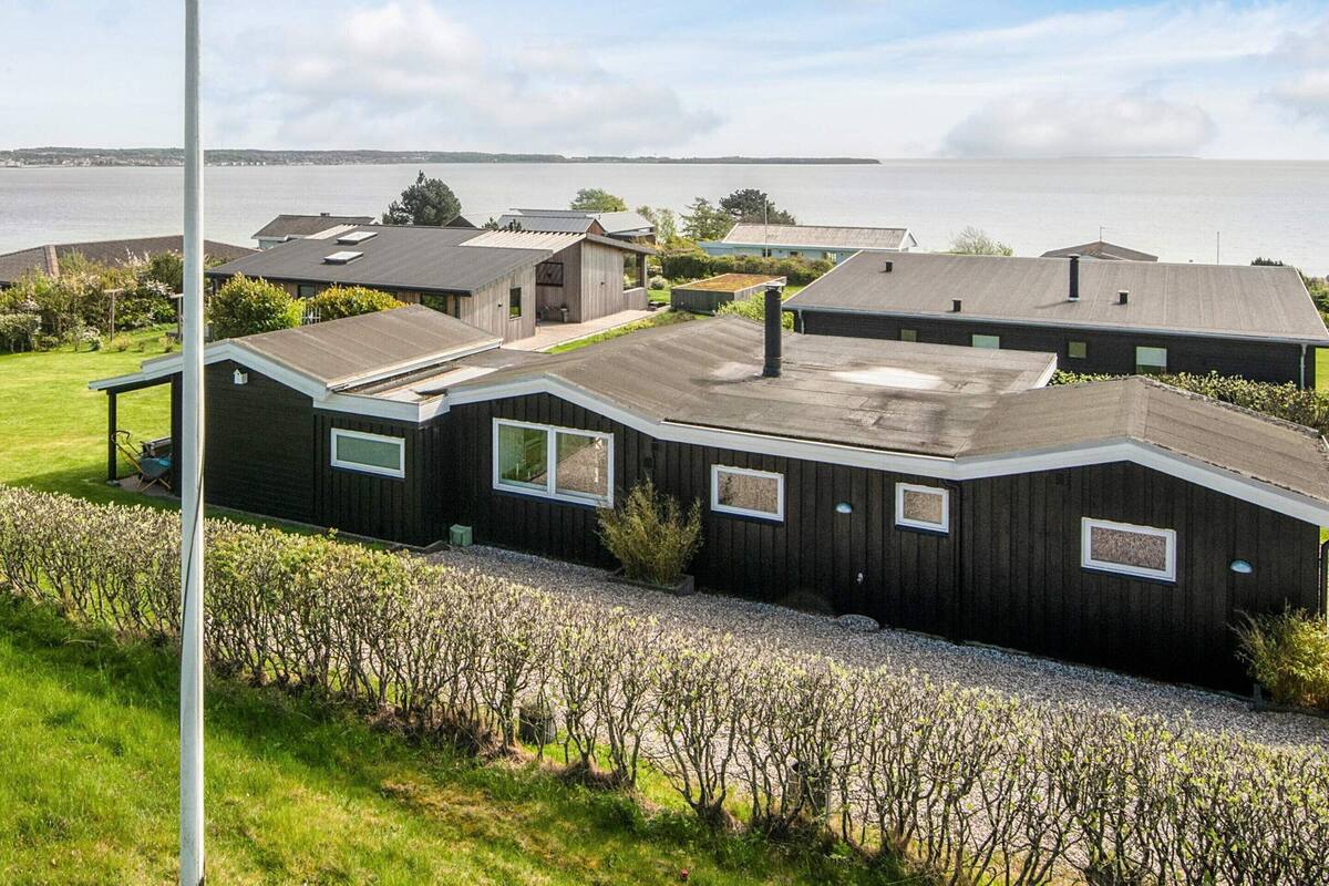 A modern house with a sloped roof, multiple windows, and a view of a body of water.