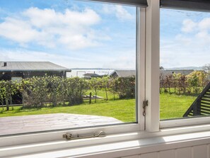 A window with a view of a grassy yard, a wooden deck, and a building with a sloped roof. - 4 Star Holiday Home in Ebeltoft (Ebeltoft)