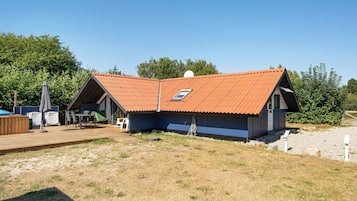 A single-story building with a sloped roof, a small attached structure, and a wooden deck with outdoor seating.