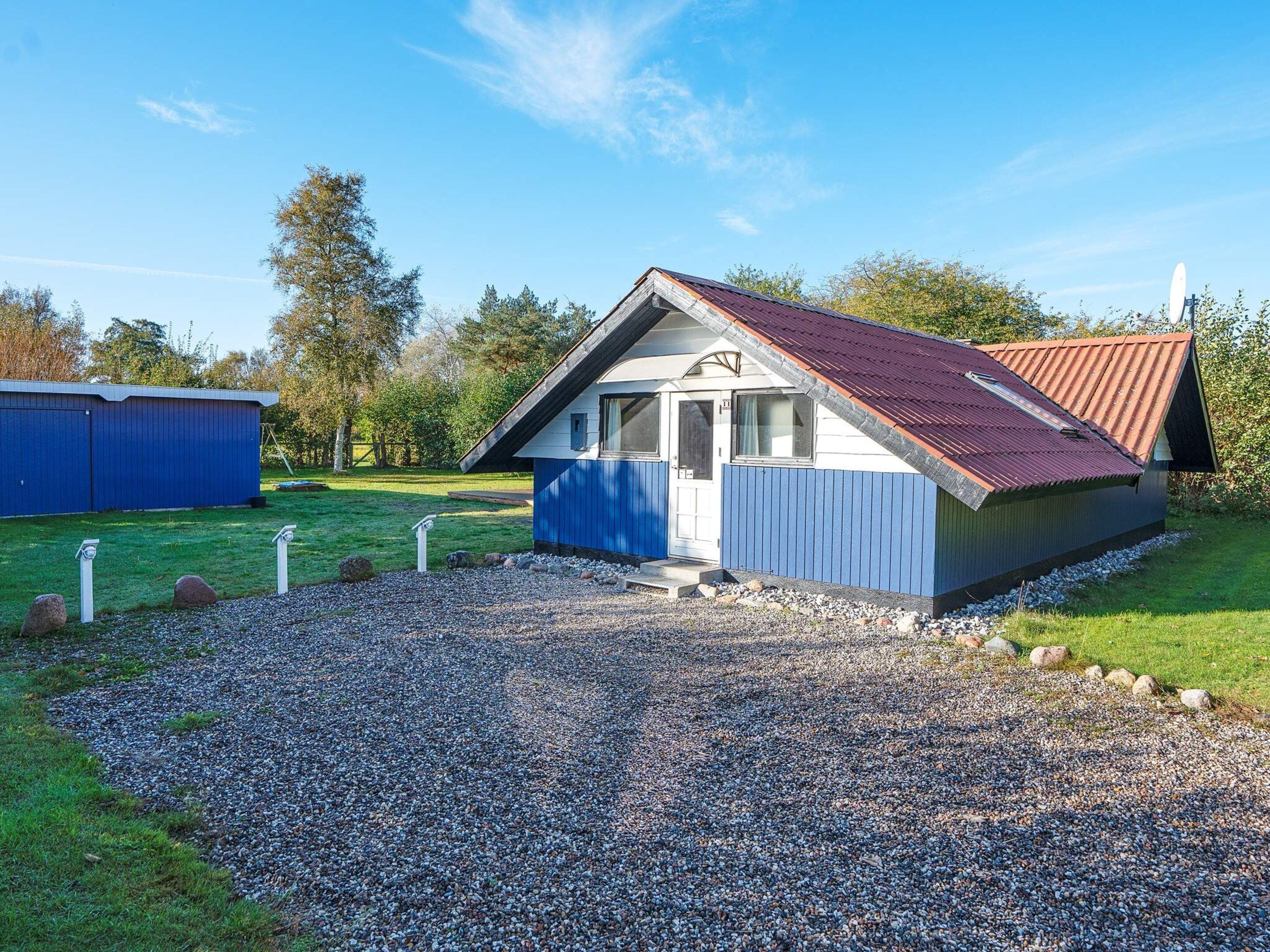 Ein kleines, eingeschossiges Gebäude mit geneigtem Dach, einer Schotterauffahrt und blauer Fassade.