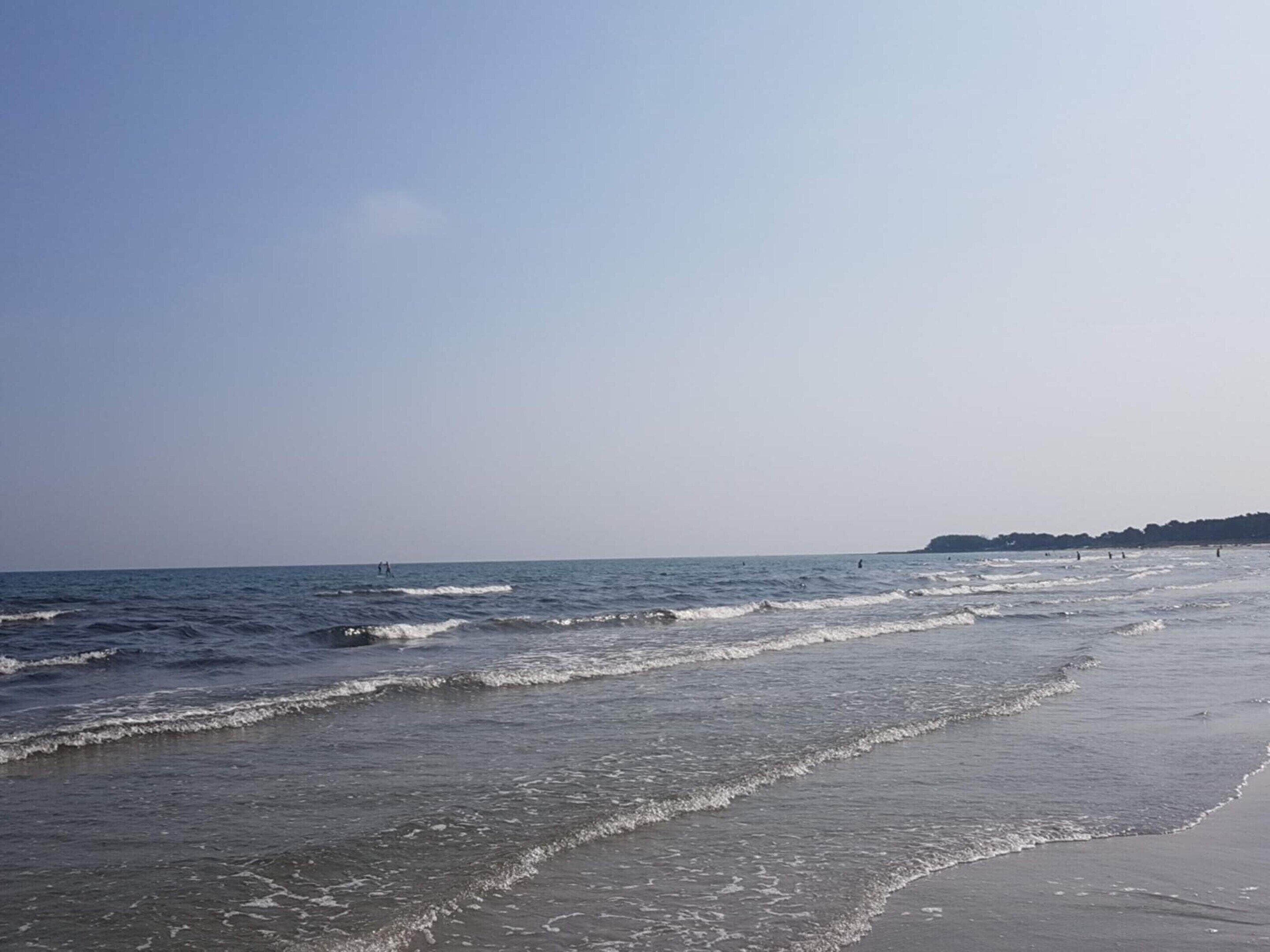 Een strand met golven, een heldere lucht en een verre kustlijn.