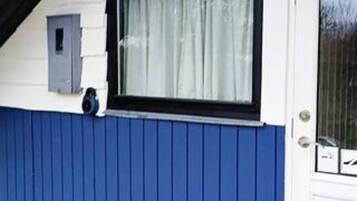 A building with a blue exterior, a window with a curtain, and a small electrical box on the wall.