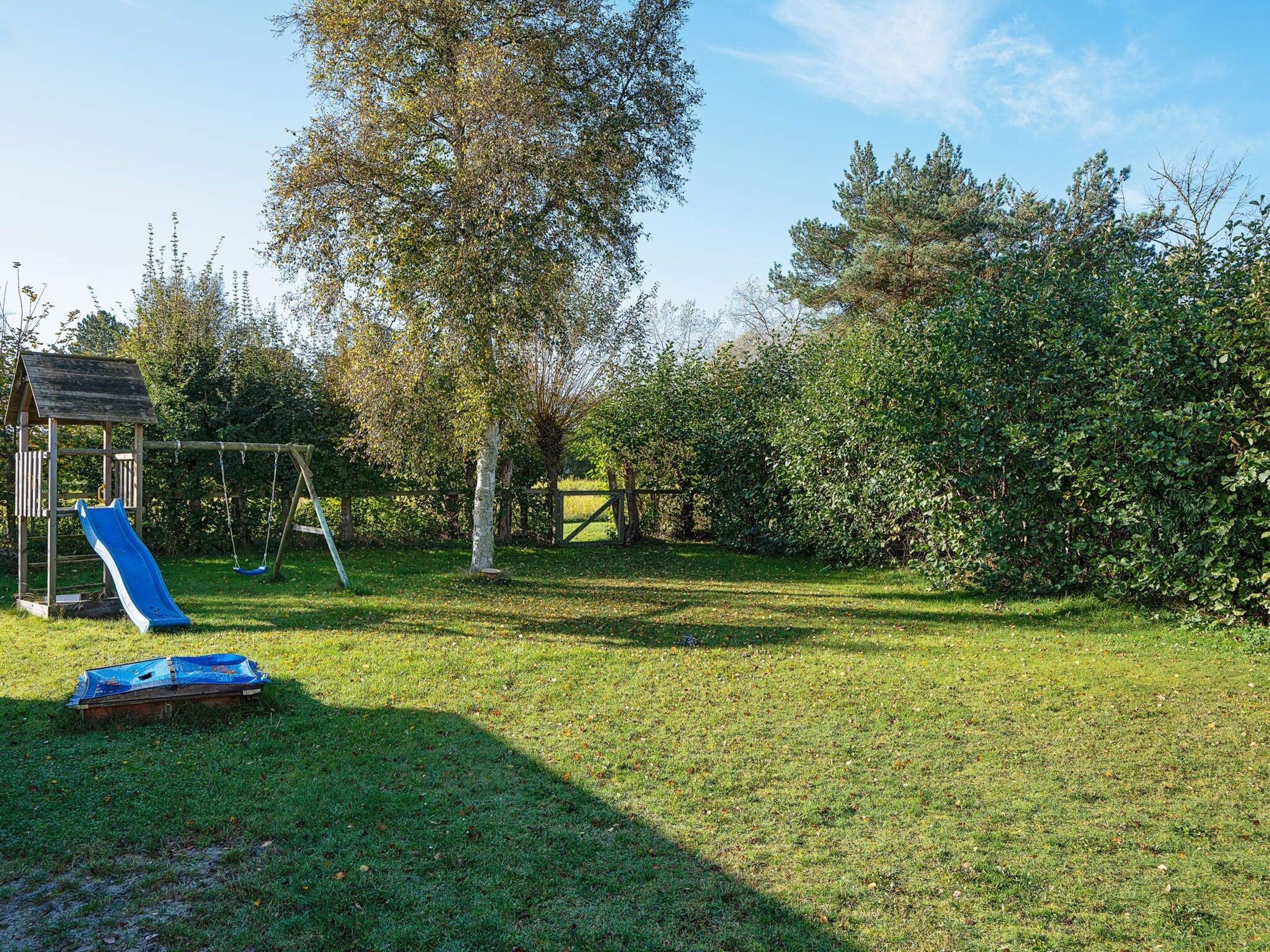 A grassy outdoor area with a wooden play structure including a slide and swings.