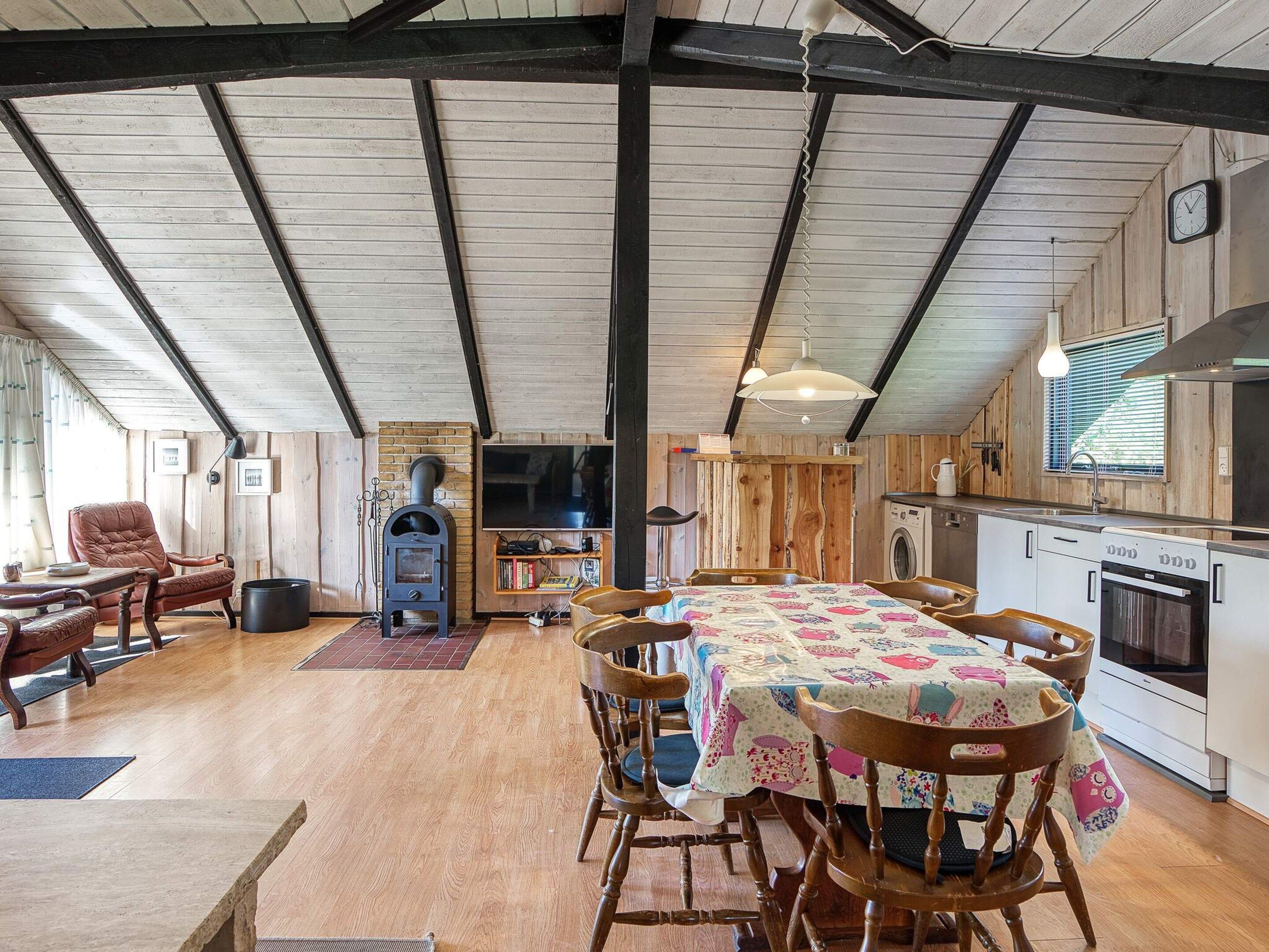 Un interior rústico con una mesa de comedor, sillas, un hogar de leña, una zona de cocina y un ventanal grande.