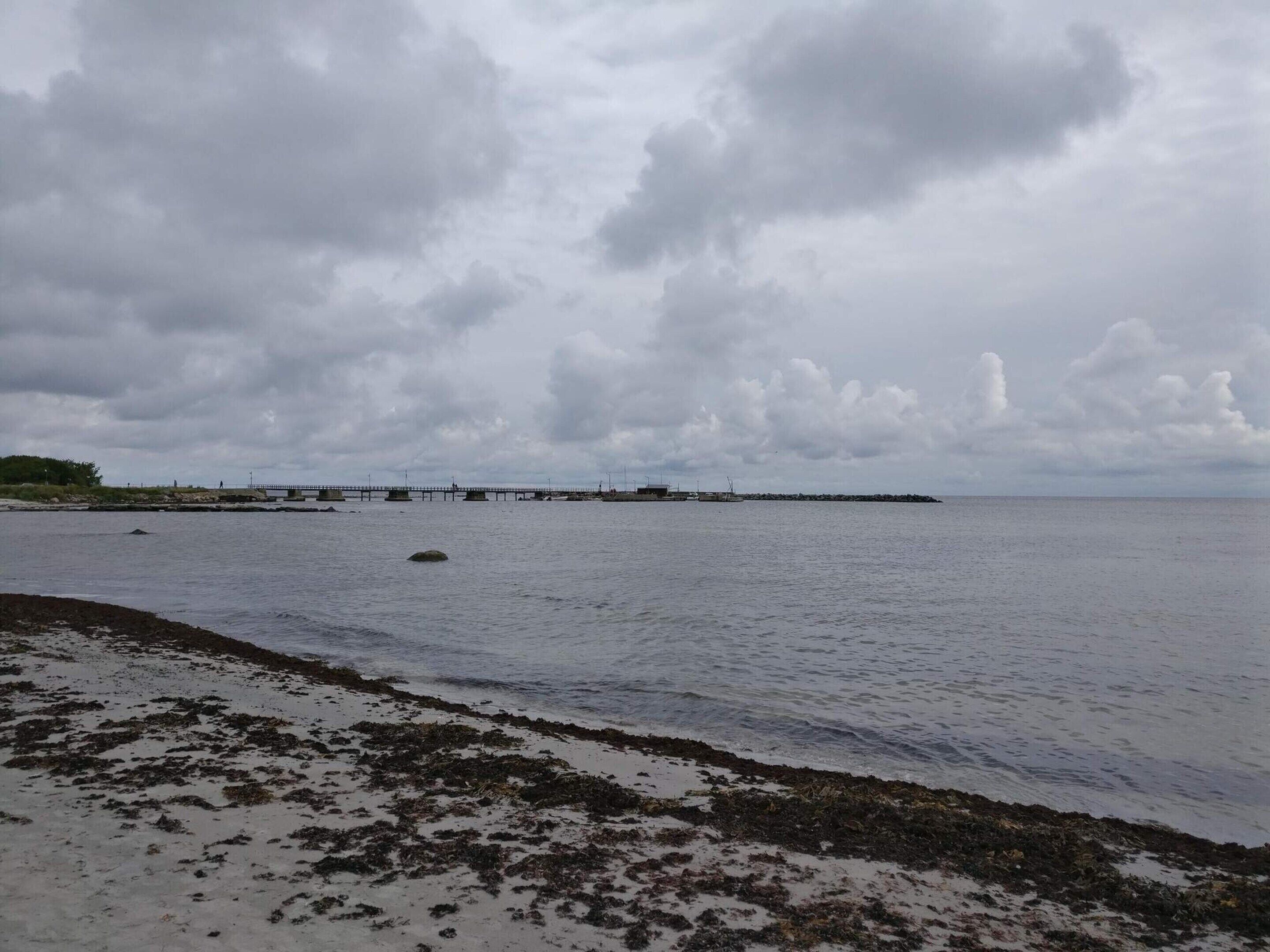 A beach with a pier extending into the water, rocky shoreline, and overcast sky.