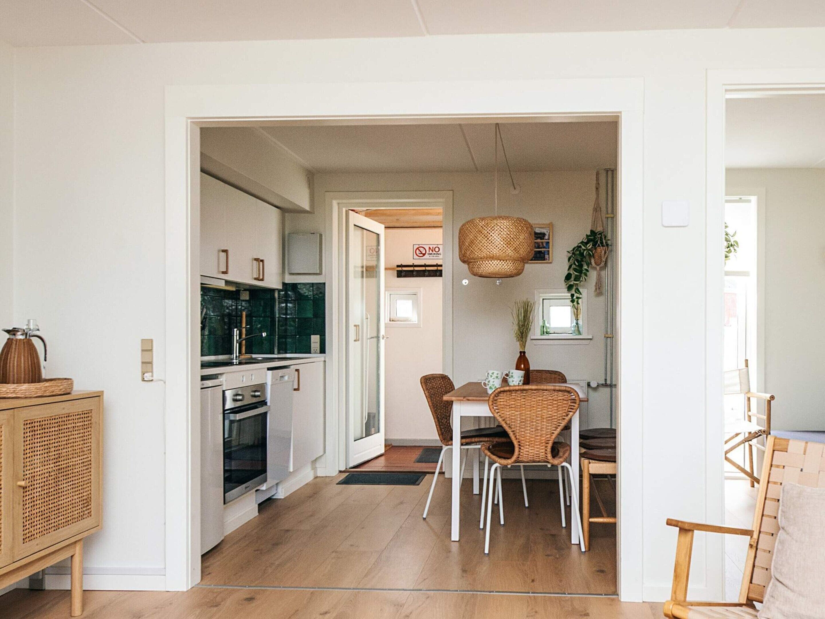 A modern kitchen with white cabinets, a built-in oven, and a dining area with wicker chairs and a table.