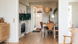 Une cuisine moderne avec des meubles blancs, un four encastré et un coin repas comprenant des chaises et une table en osier.
