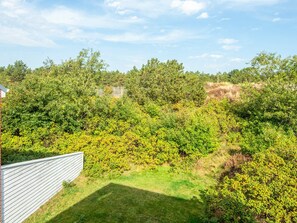 A landscaped garden with a variety of shrubs and trees, a wooden fence, and a clear sky.