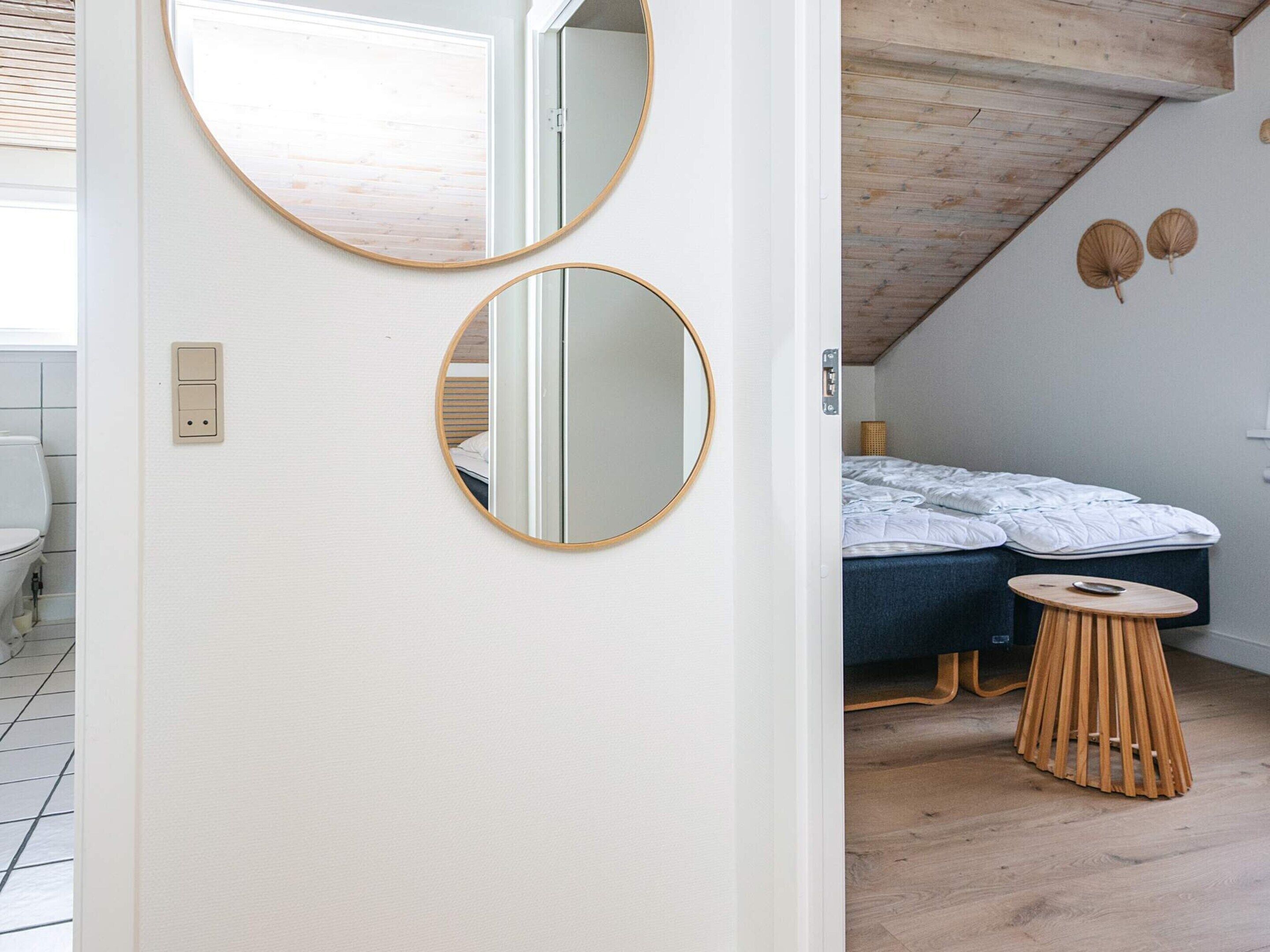 A room with a bed, a round mirror, and a small wooden stool.