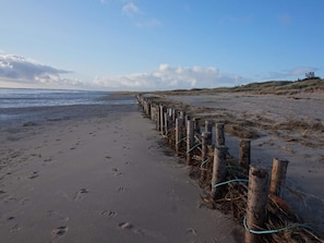 Ein Sandstrand mit Holzpfählen, Seilen, Fußspuren und blauem Himmel.