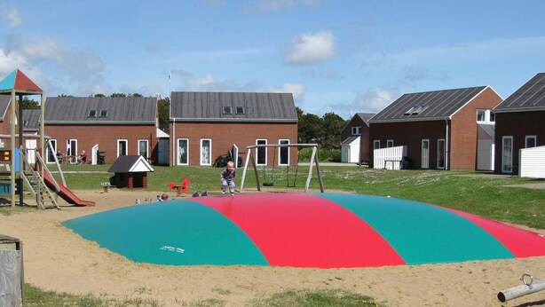 Un terrain de jeux avec une aire de jeux colorée, comprenant un toboggan et des balançoires, situé devant des immeubles d’habitation.