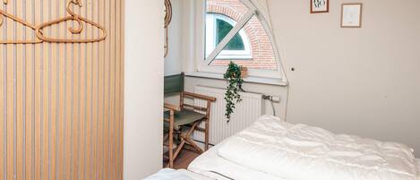 Quarto com cama, janela com vista para um edifício de tijolos e teto de madeira.