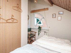 Et soveværelse med seng, et vindue der udover til en murstensbygning, og et træloft.