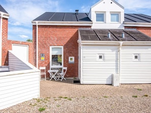 A two-story building with a brick facade, a garage with two doors, and a small patio area with a table and chairs. - 6 Person Holiday Home in Romo (Rømø)