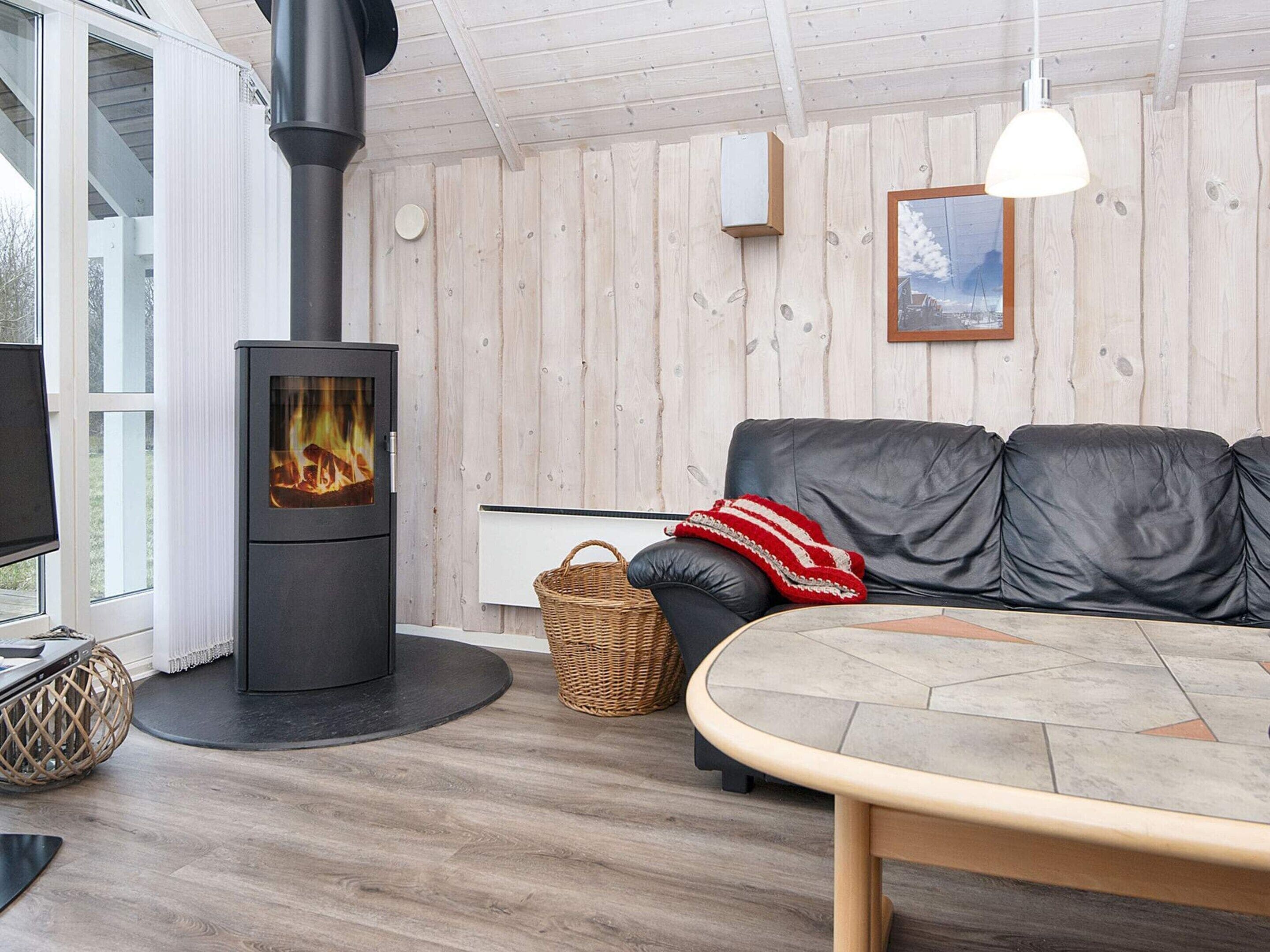 Un salon chaleureux avec un poêle à bois noir, un canapé en cuir noir, un panier en osier et une table ronde en bois.