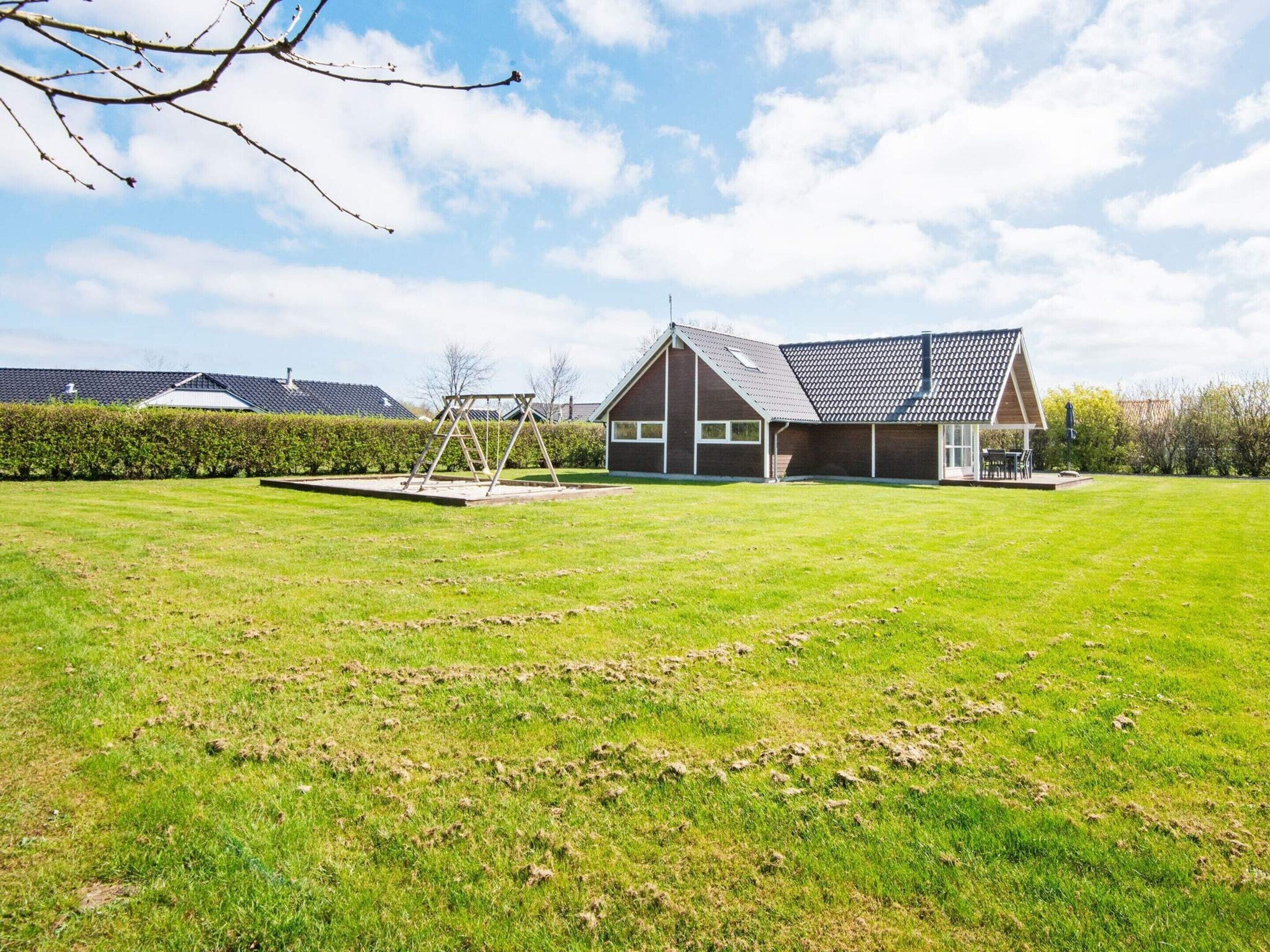 A modern house with a large lawn, a swing set, and a small patio area.