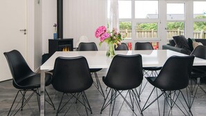 A dining area with a white table, black chairs, a black heater, and a vase with pink flowers.