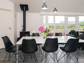 A dining area with a white table, black chairs, a black heater, and a vase with pink flowers. - 8 Person Holiday Home in Ringkobing (Ringkobing)
